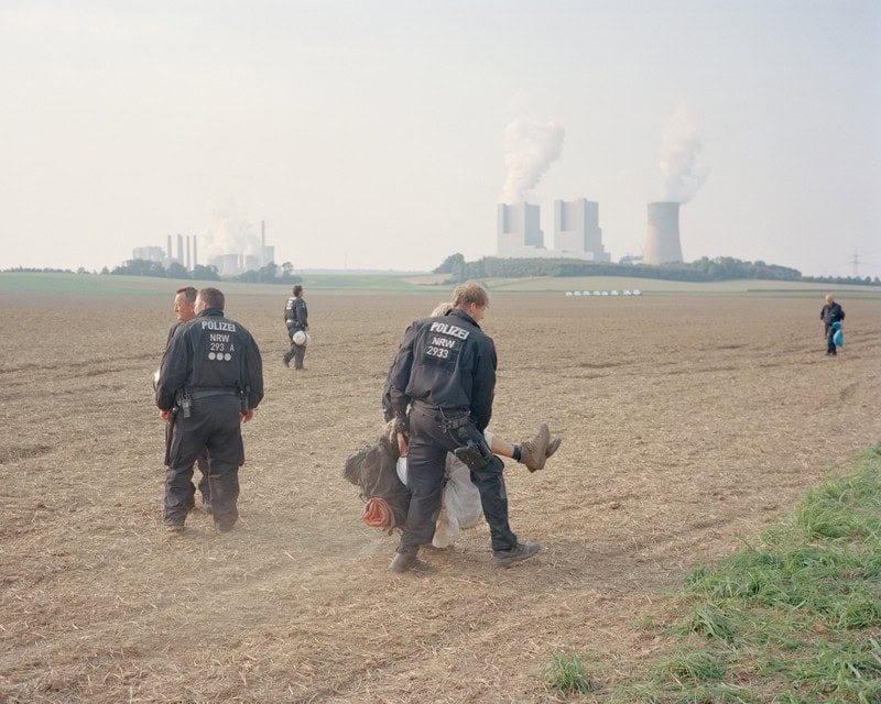 Polizisten tragen auf einem Feld Demonstrant:innen weg