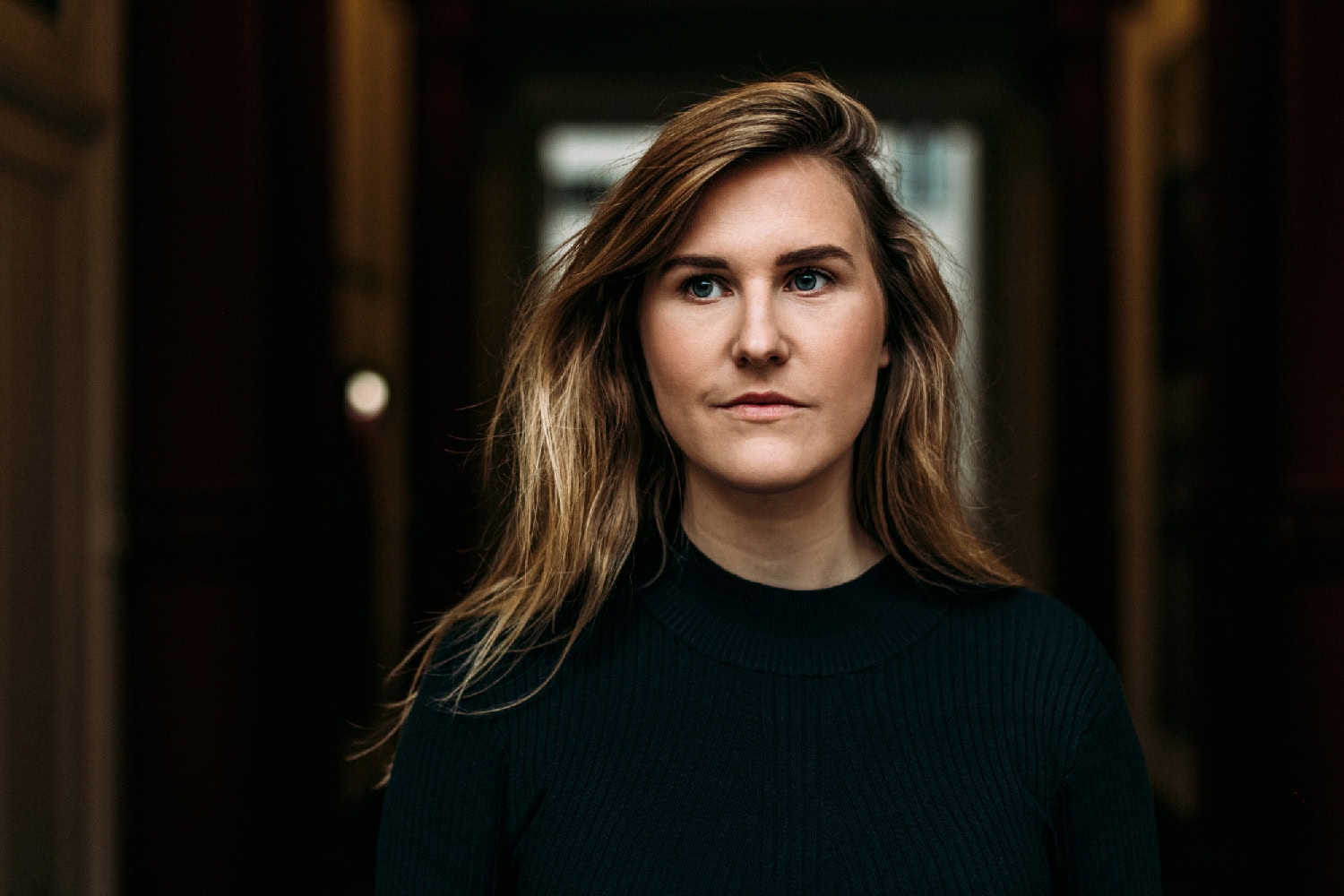 Natürliche Frauenporträtaufnahme in dunkler Umgebung, Mode und Schönheit, professionelle Fotografie, leicht unscharfer Hintergrund.