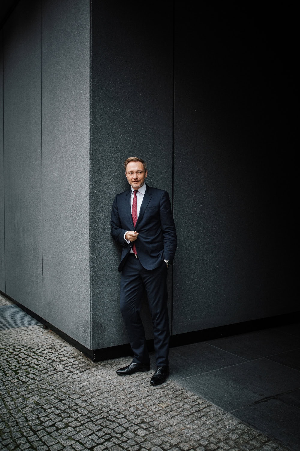 Eleganter Geschäftsmann in dunklem Anzug vor modernen schwarzen Wänden.