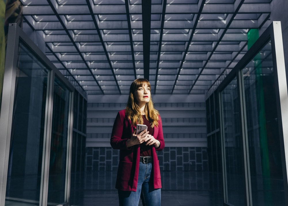 Hübsche junge Frau mit Smartphone in moderner, großflächiger Architektur in Berlin.