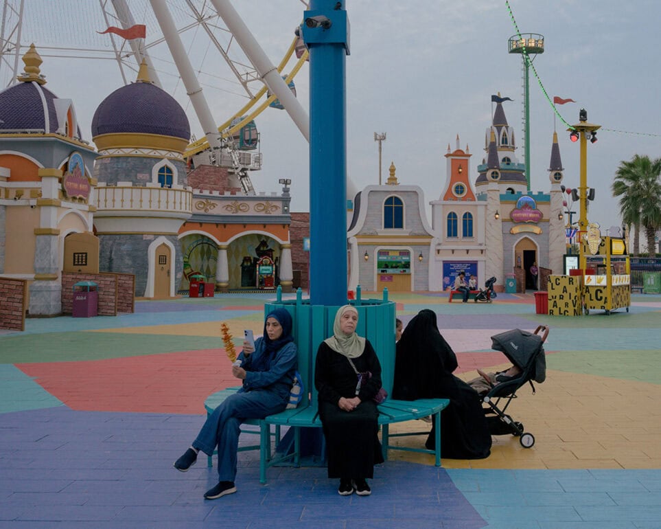 Bunte Freizeitpark-Szene mit Frauen, Kind und Karussell im Hintergrund.