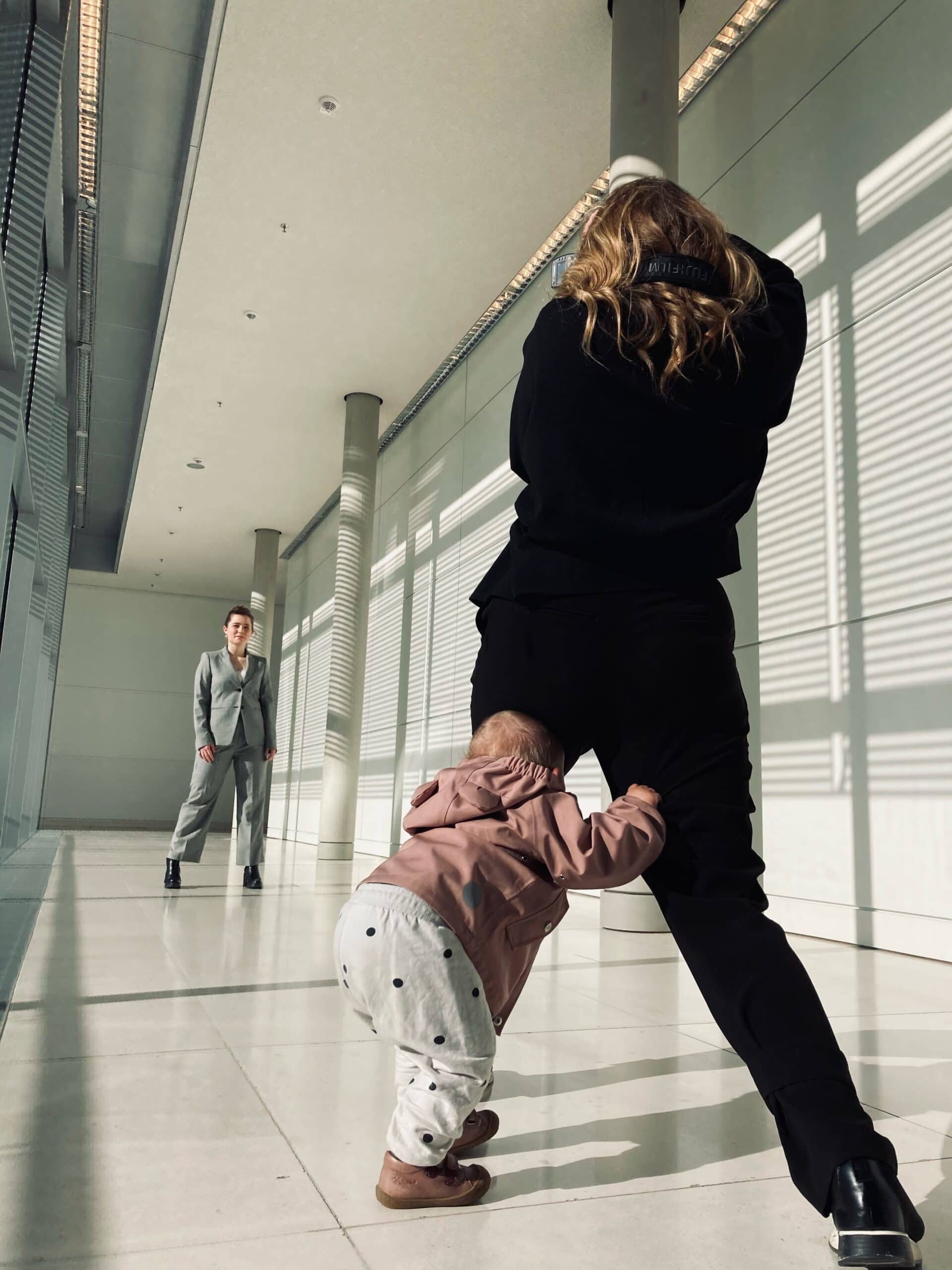 Kleinkind umarmt schwangere Frau in moderner, heller Architektur.